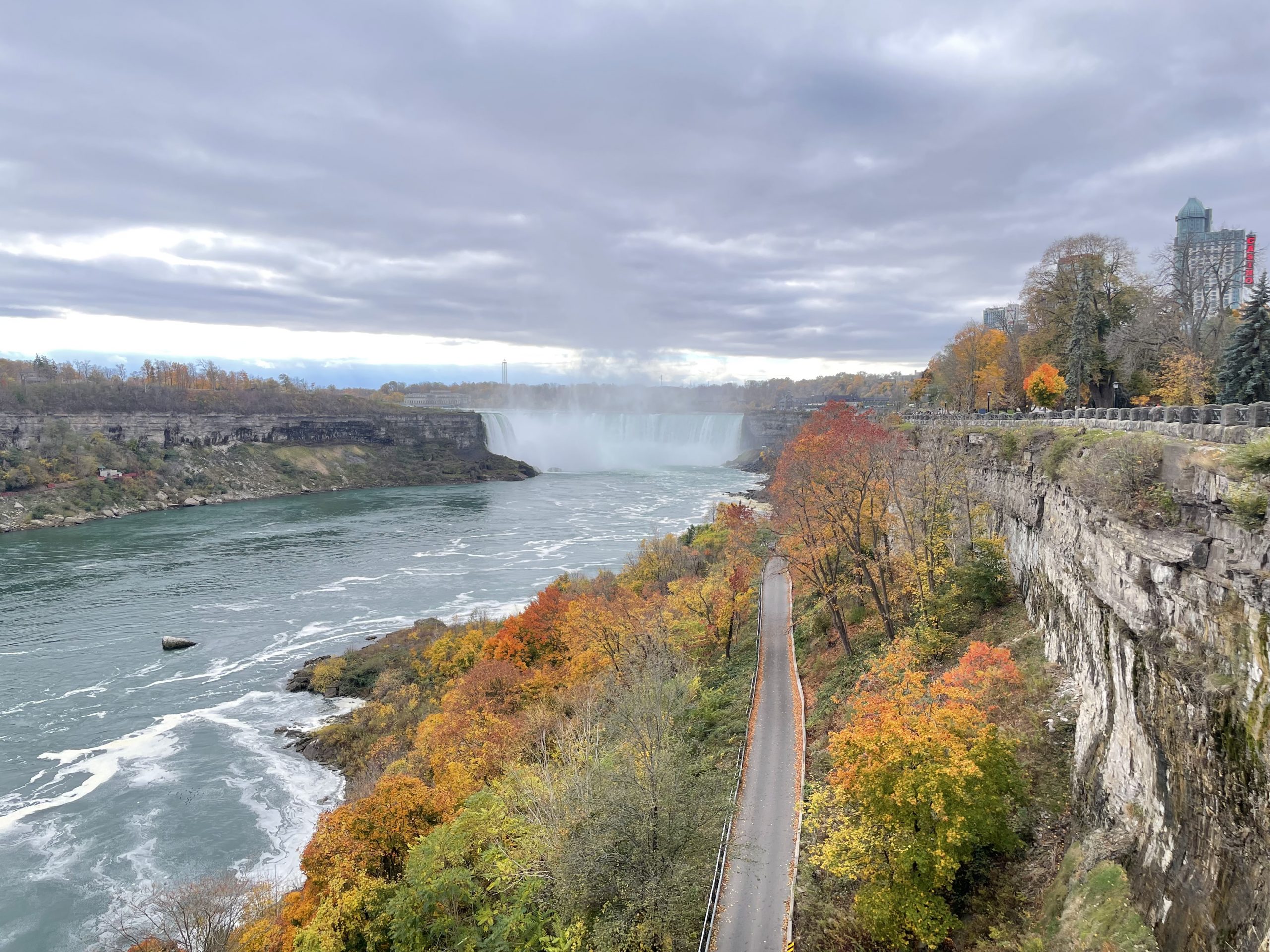 Niagarafälle aus der Ferne. Bunt gefärbte Bäume im Vordergrund. Bewölkter Himmel