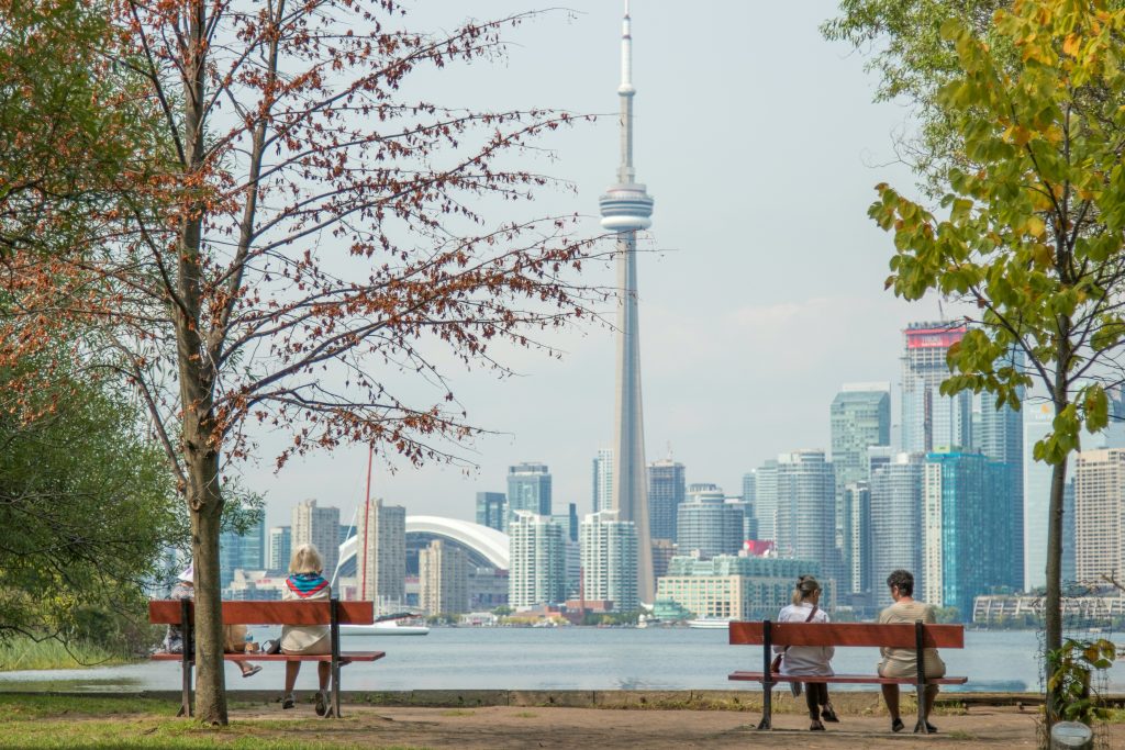 Menschen auf Sitzbänken in einem Park schauen auf die Skyline von Toronto