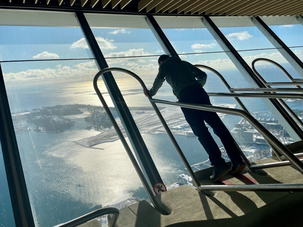 Mann lehnt in Fenster im CN Tower und schaut auf die Toronto Islands.
